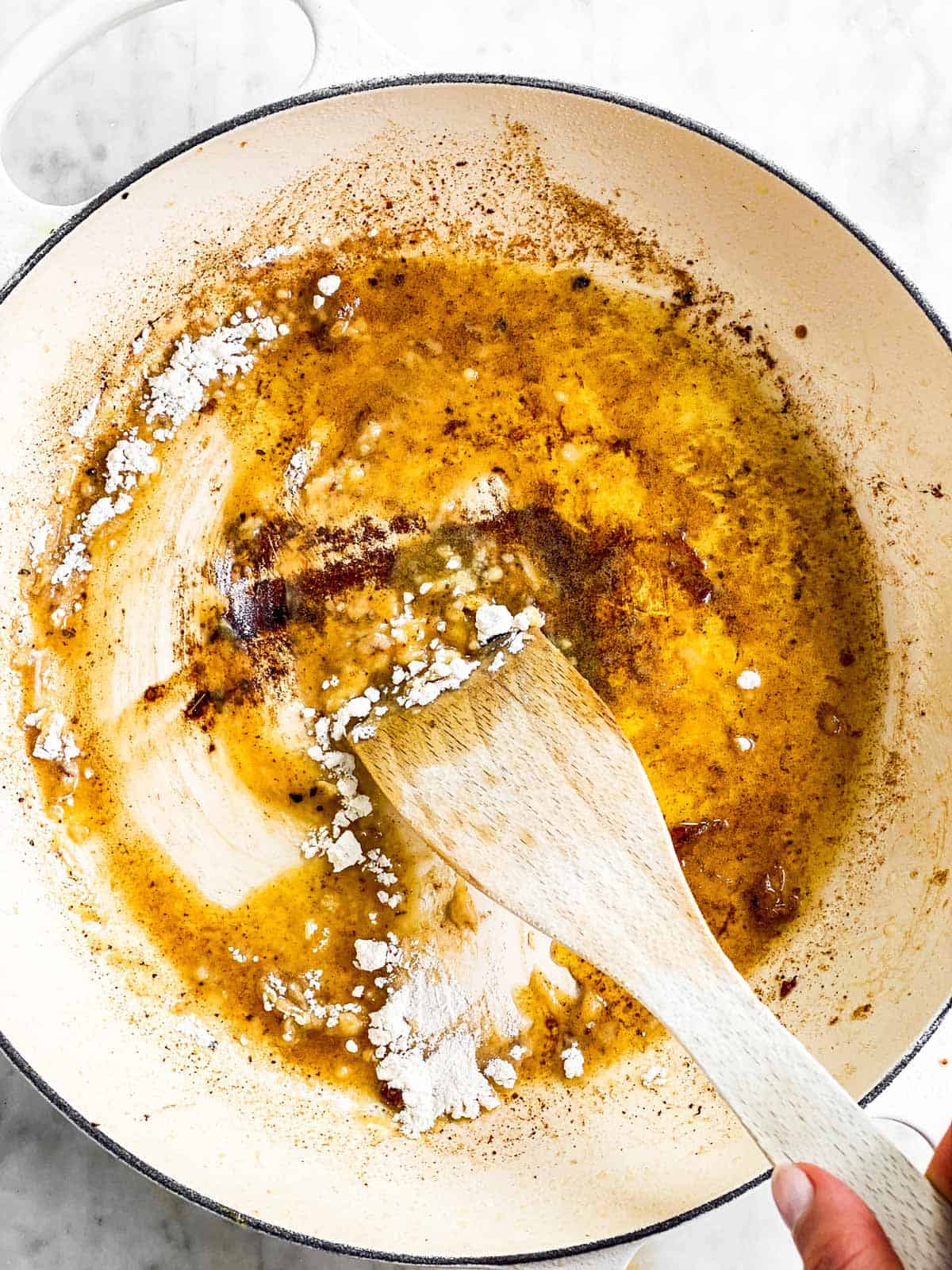 female hand using wooden spatula to stir flour into melted butter