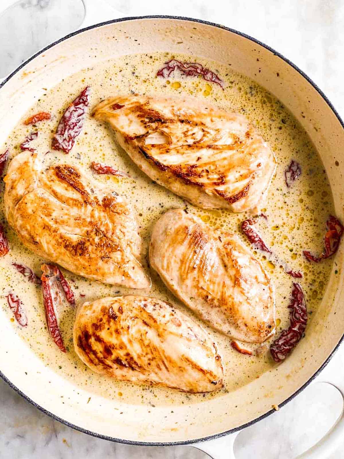 cooked chicken breasts in creamy sauce in white cast iron skillet