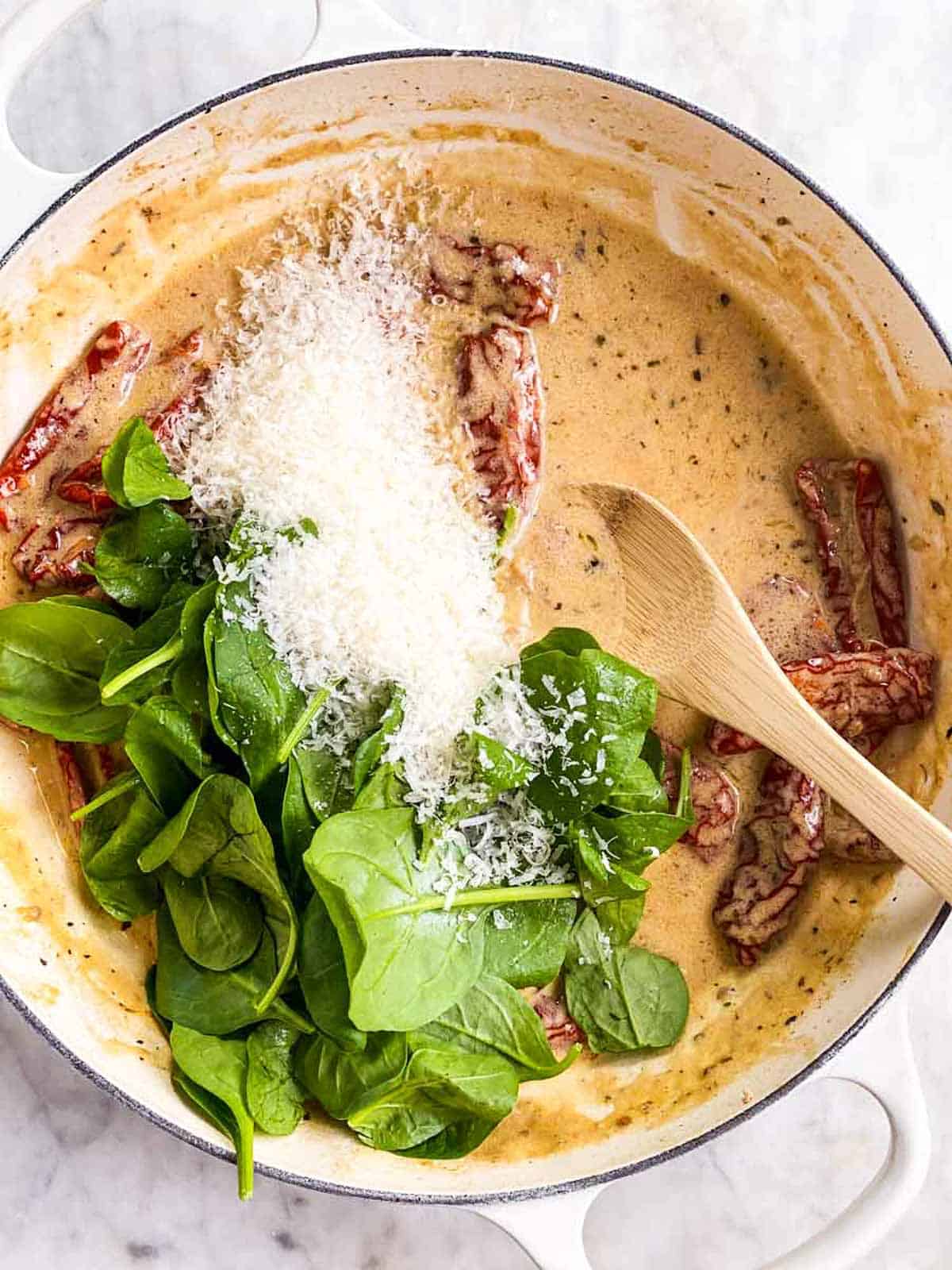 cream sauce in white skillet with fresh baby spinach and grated parmesan cheese