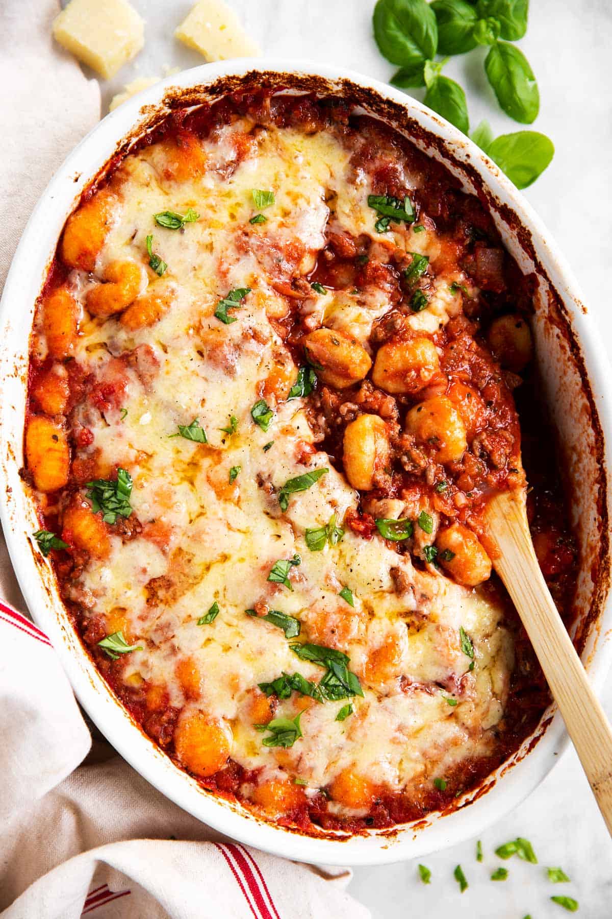 overhead view of white casserole dish with baked gnocchi on marble surface, with wooden spoon stuck in casserole