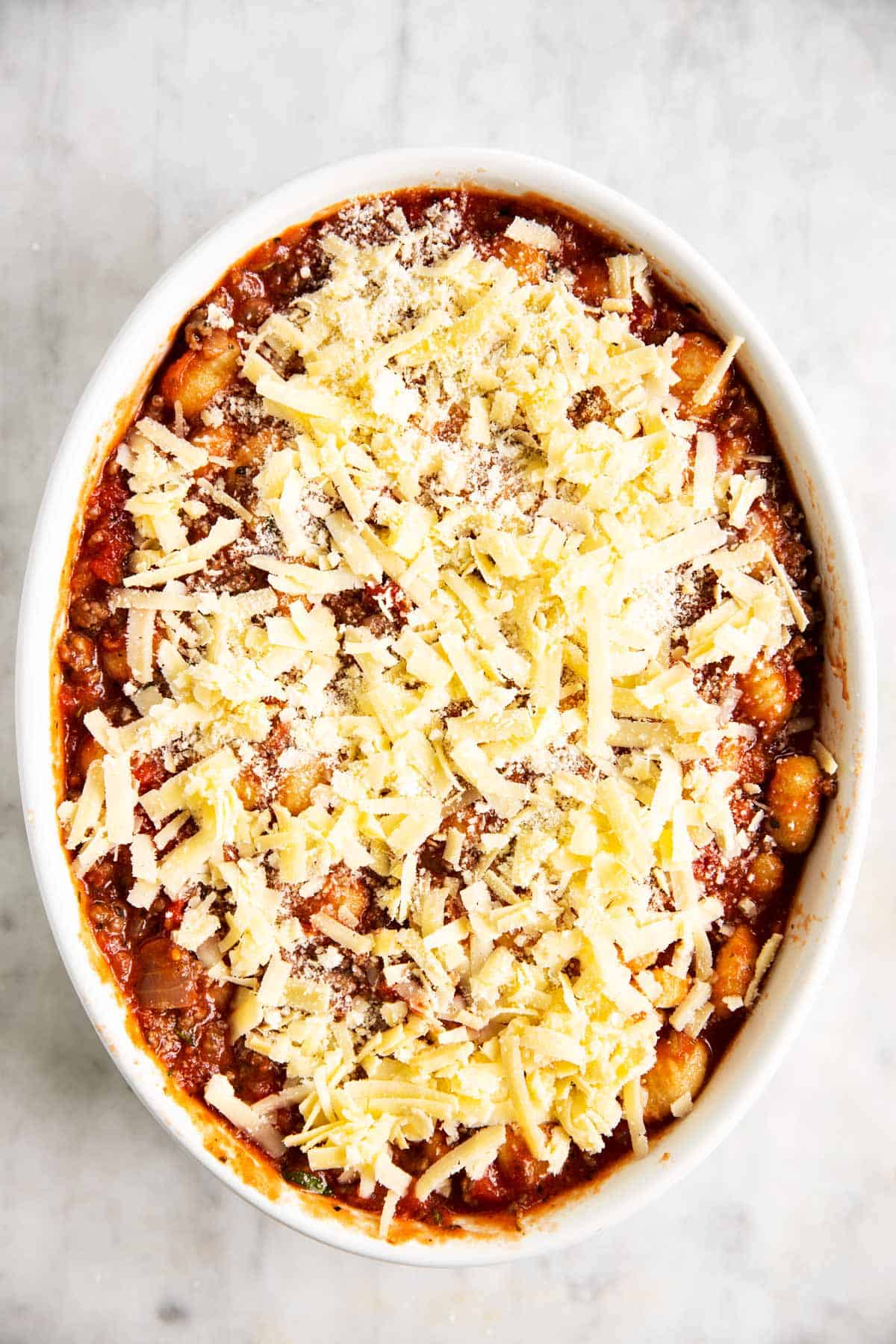 gnocchi, ground beef and tomato sauce mixture in white casserole dish covered with cheese