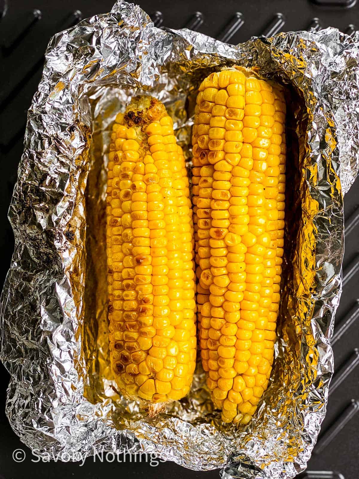 charred corn on the cob in opened foil packet on grill