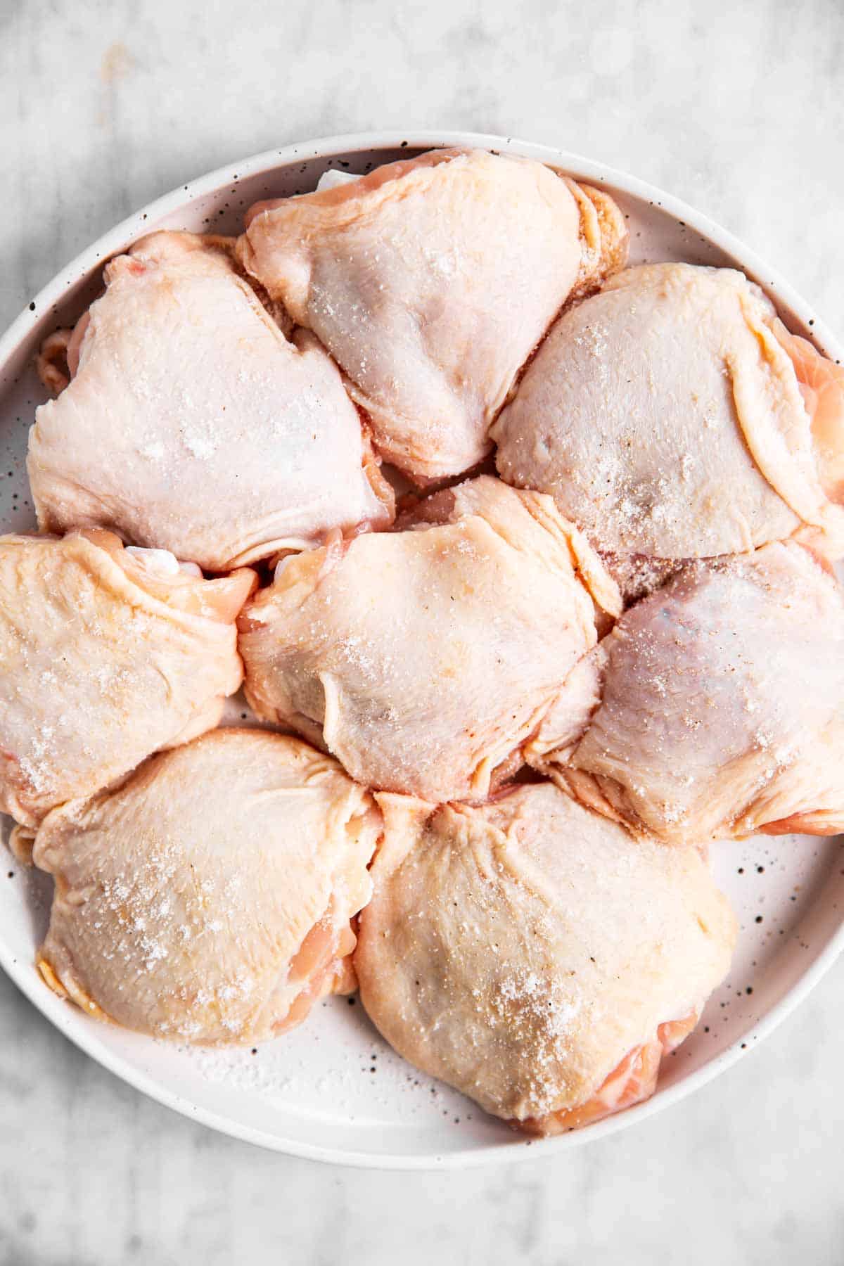 eight raw chicken thighs on white plate