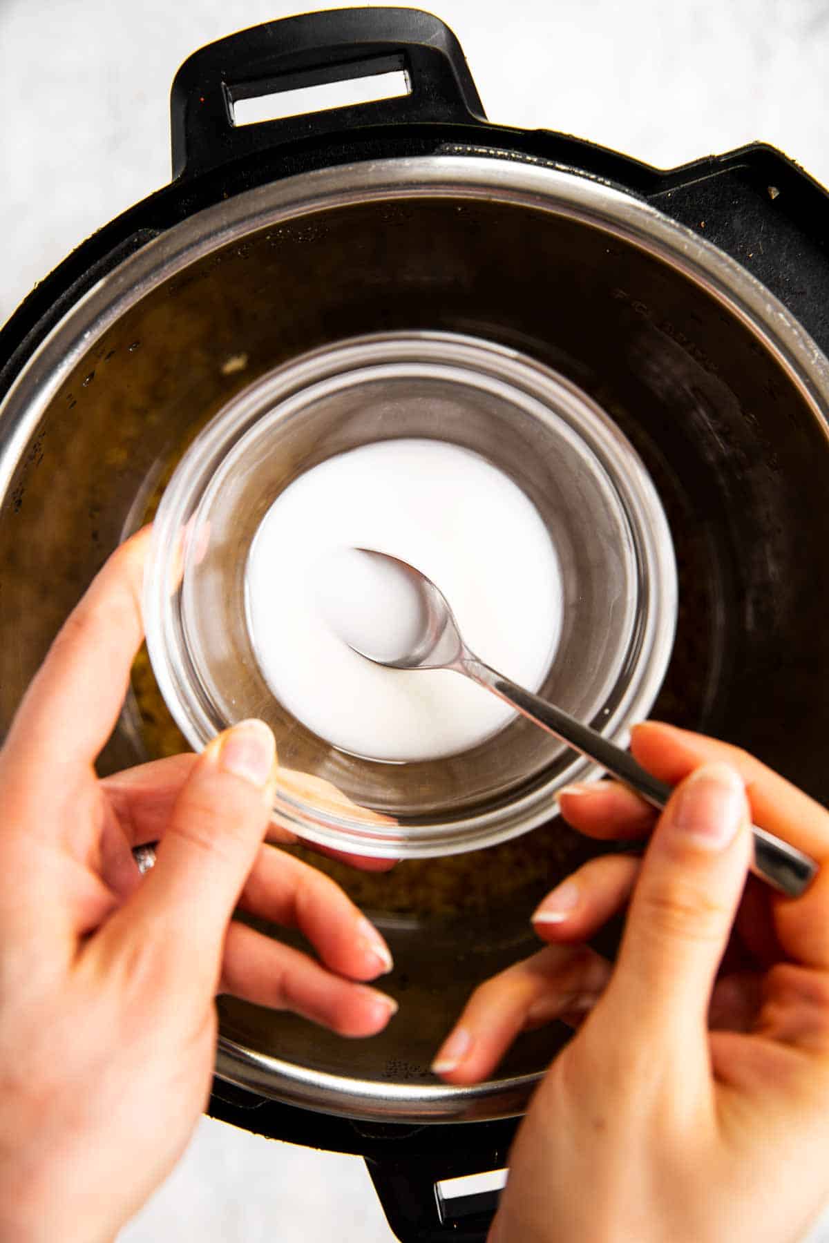 female hands holding glass bowl with cornstarch slurry, with teaspoon inside
