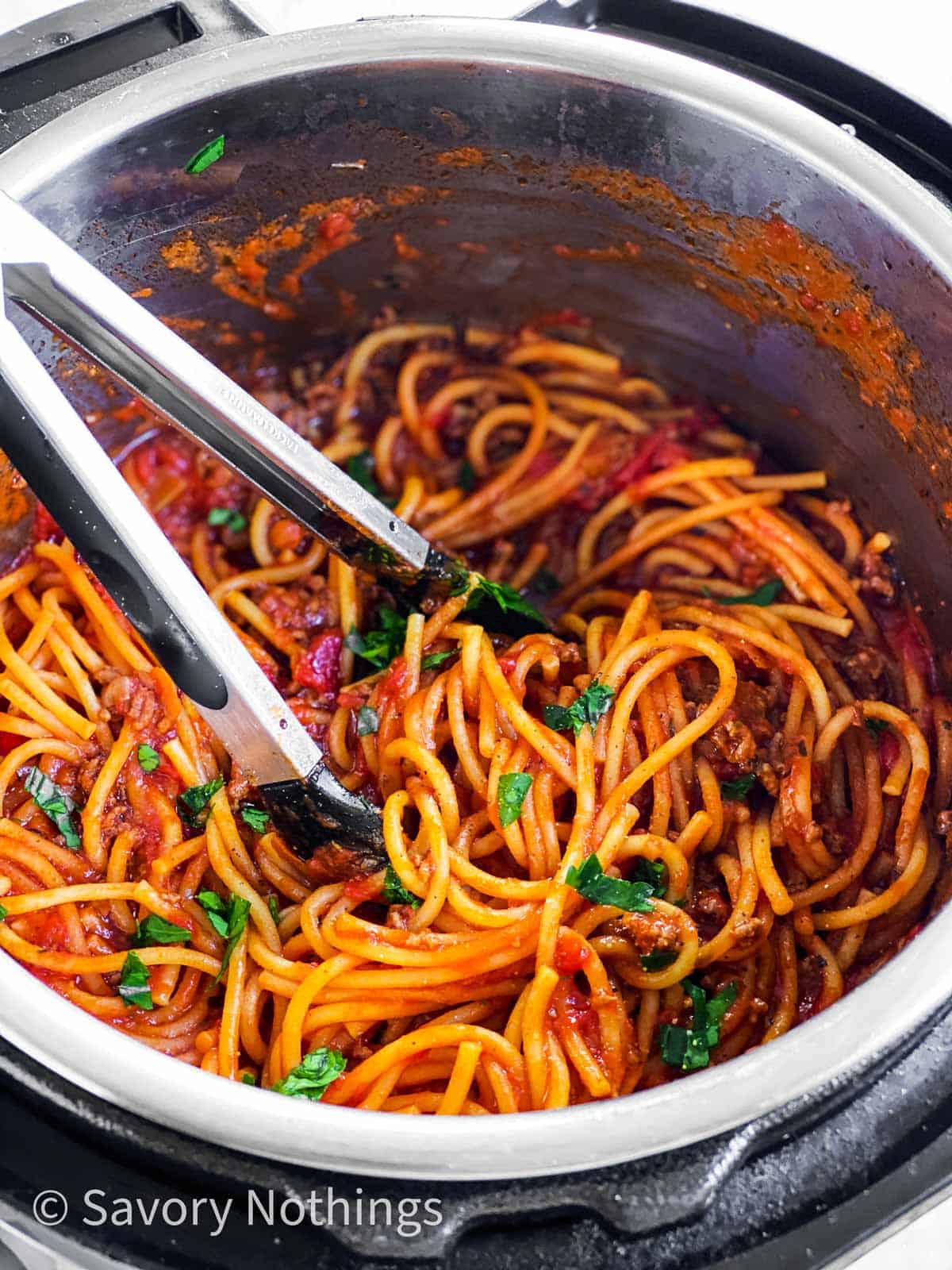 frontal view of spaghetti and meat sauce in instant pot with kitchen tongs