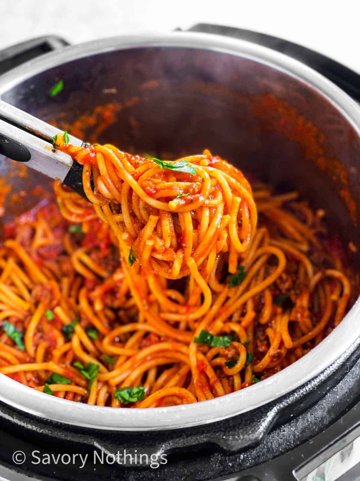 kitchen tongs scooping spaghetti and meat sauce from instant pot