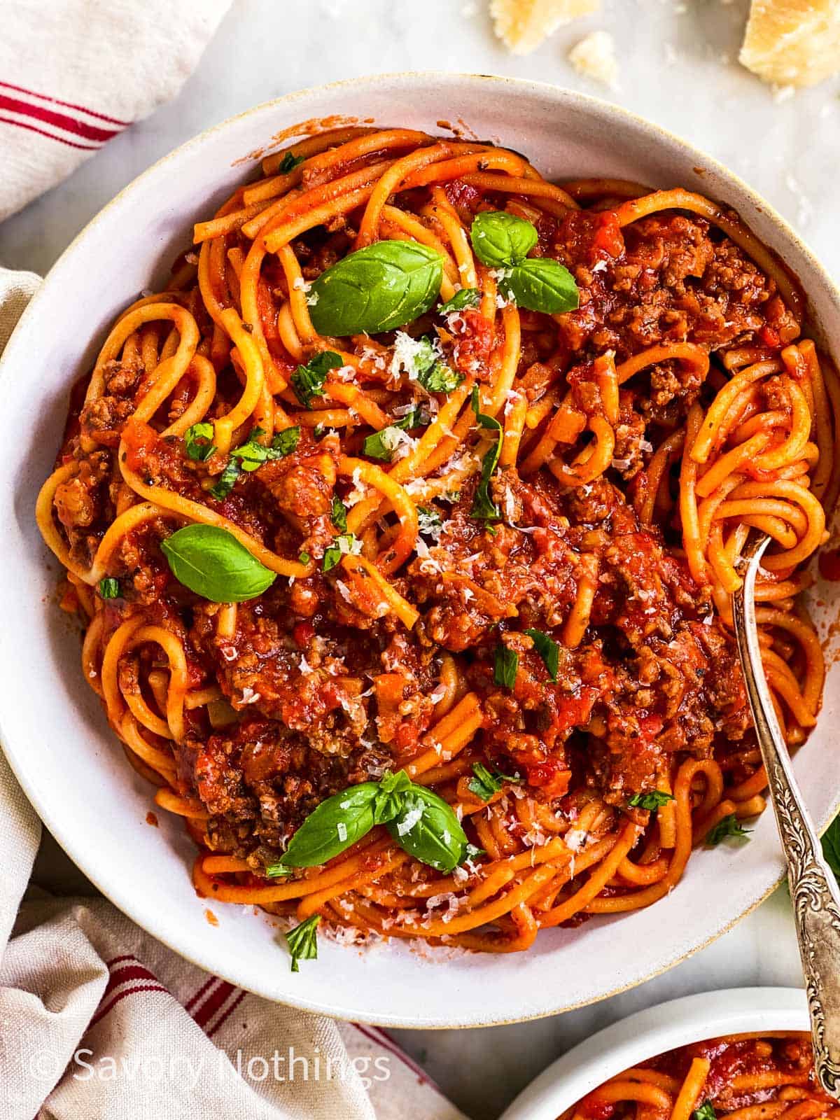 close up photo of white plate filled with spaghetti and meat sauce and garnished with fresh basil