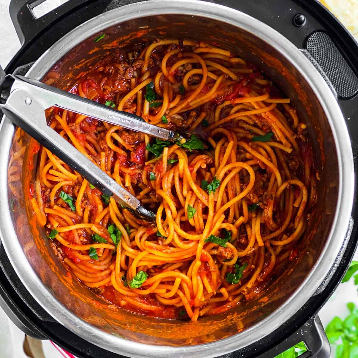 overhead view of instant pot filled with spaghetti and meat sauce with kitchen tongs stuck in