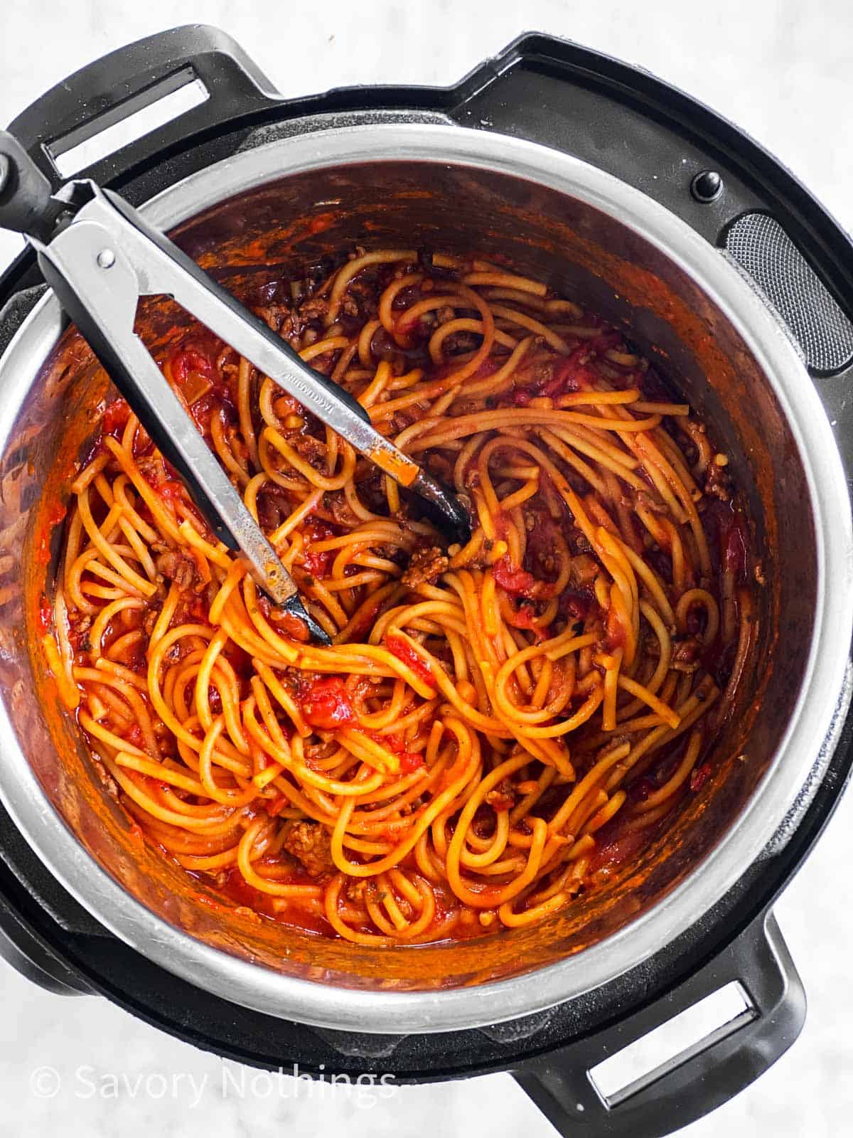 cooked spaghetti in meat sauce in instant pot with kitchen tongs