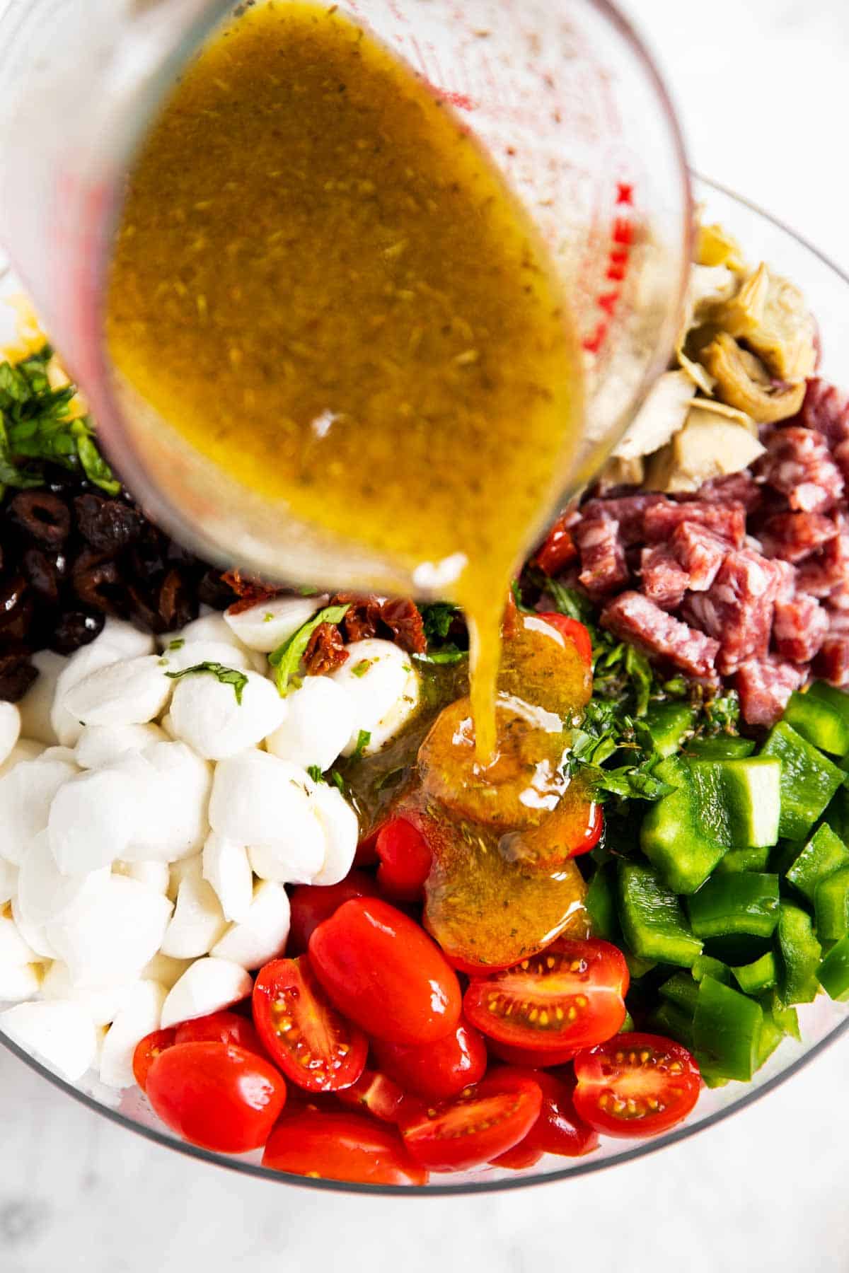 Italian dressing pouring from glass measuring jug over salad ingredients in glass bowl