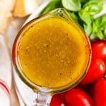 overhead view of italian dressing in glass measuring jug on white plate with tomatoes, basil and parmesan cheese