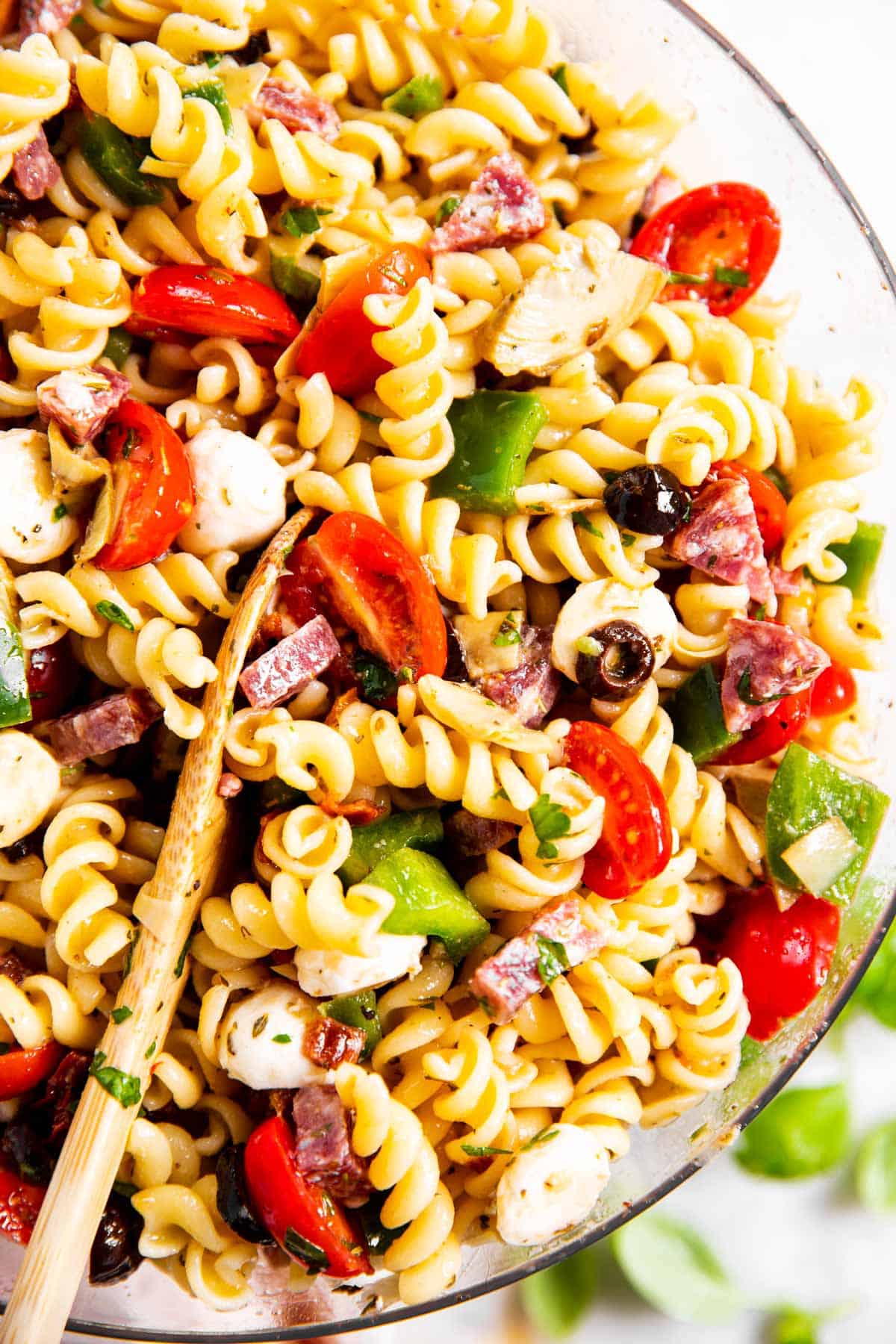 overhead close up photo of Italian pasta salad in glass bowl with wooden spoon inside salad