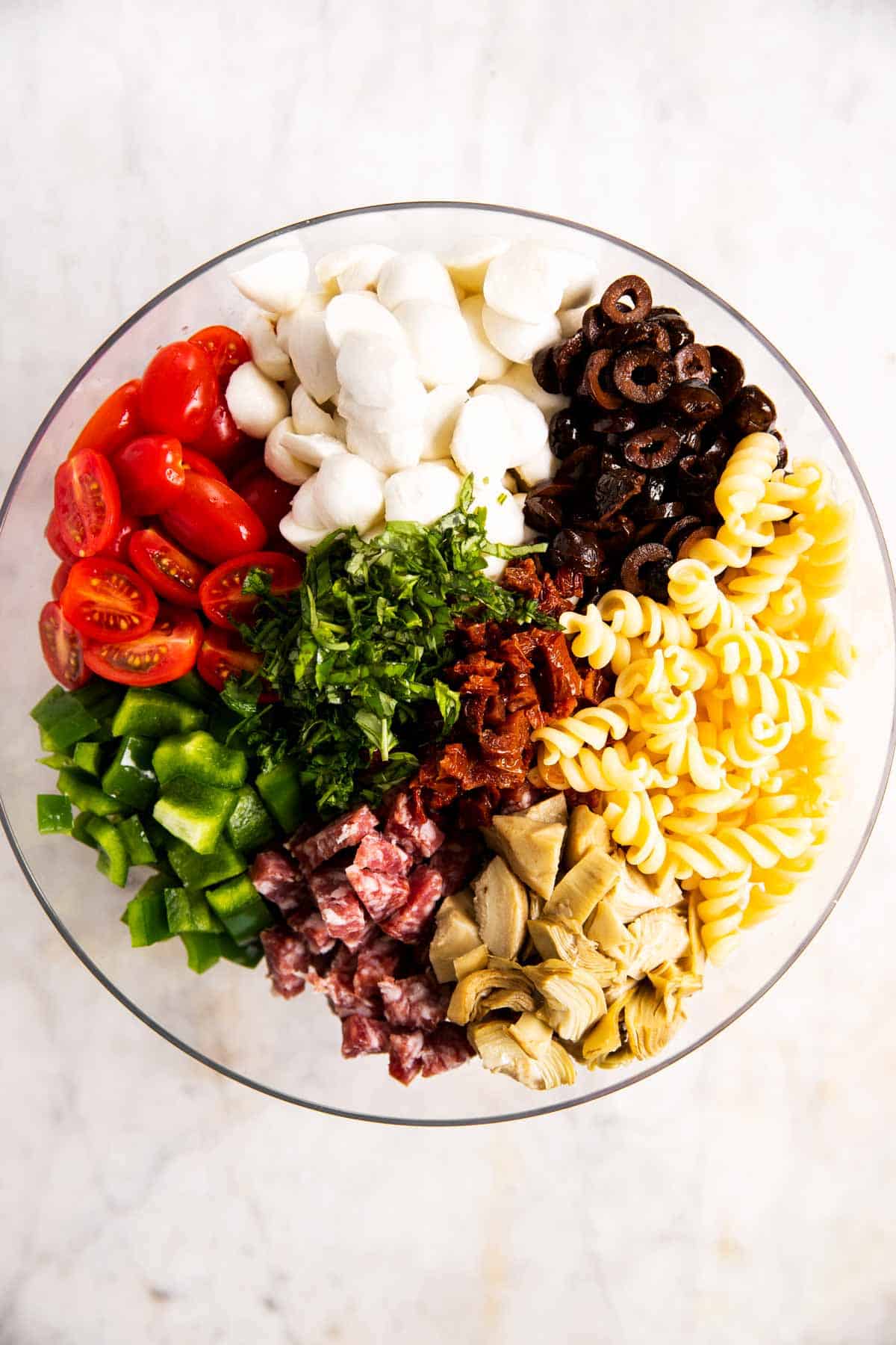 overhead view of ingredients for Italian pasta salad arranged in glass bowl