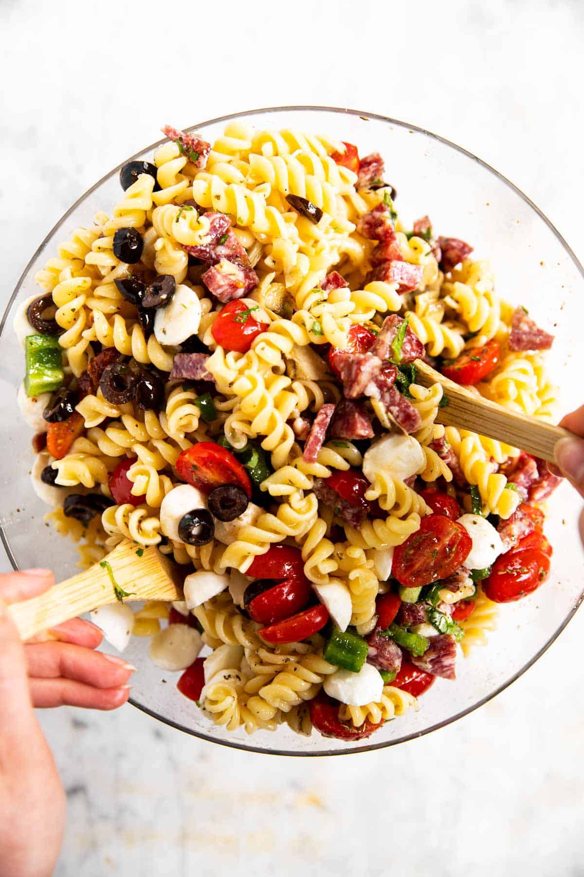 female hands using wooden salad tongs to toss Italian pasta salad in glass bowl