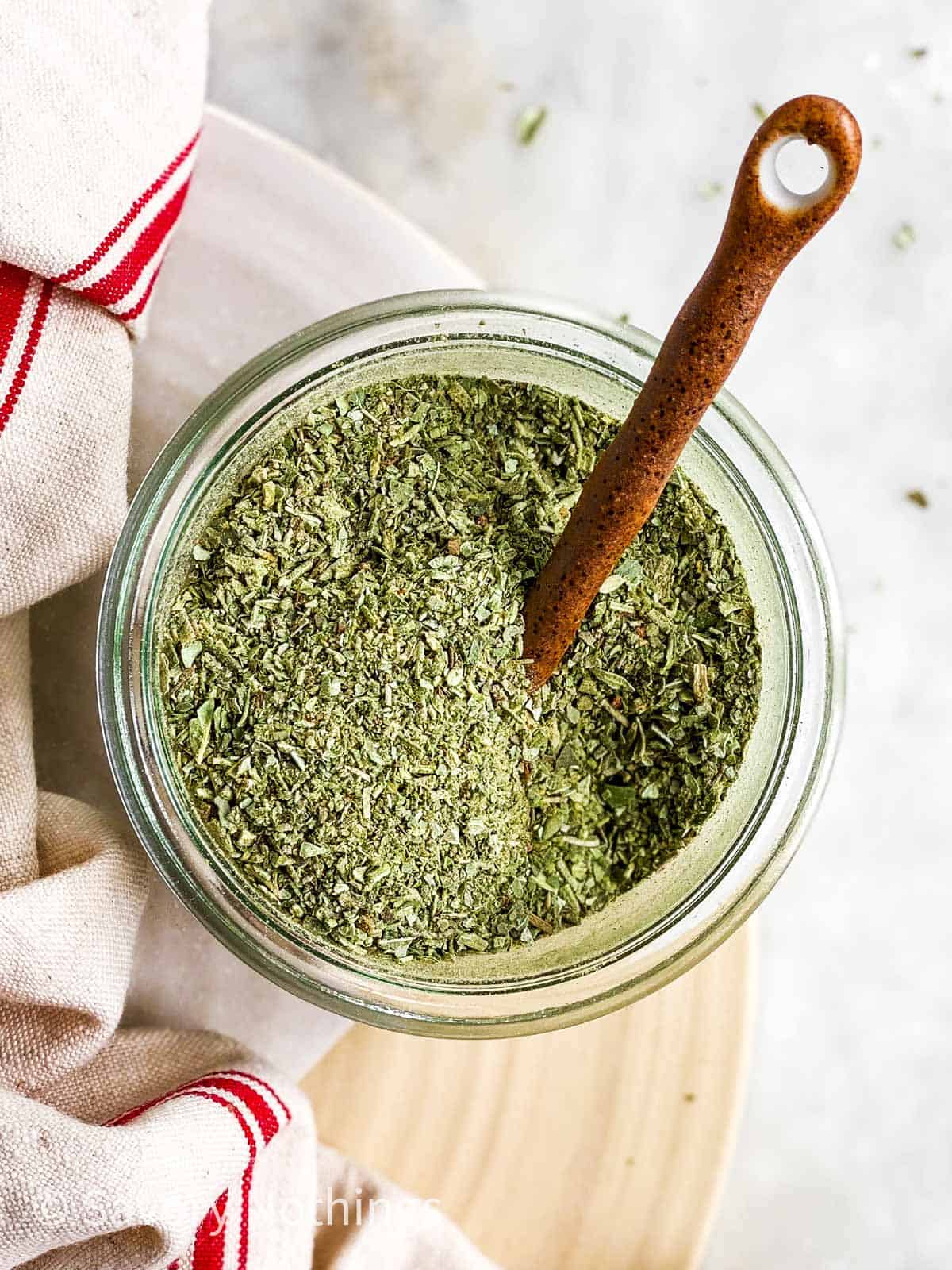 overhead view of homemade Italian seasoning in small glass jar with ceramic spoon