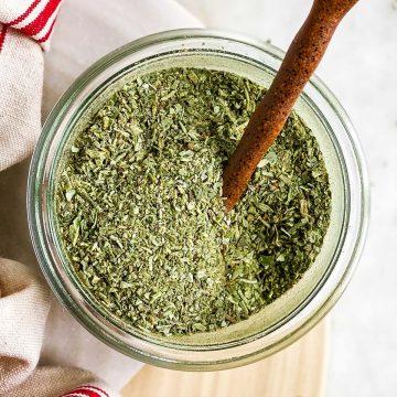 overhead view of homemade Italian seasoning in small glass jar with ceramic spoon