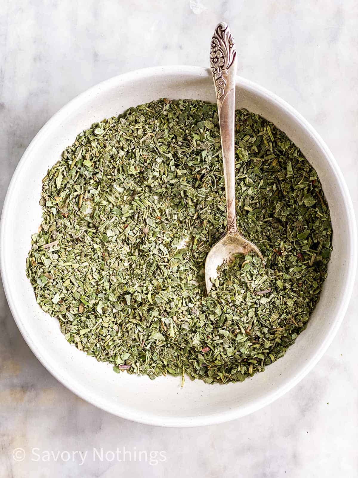 homemade Italian seasoning in white bowl with a silver spoon