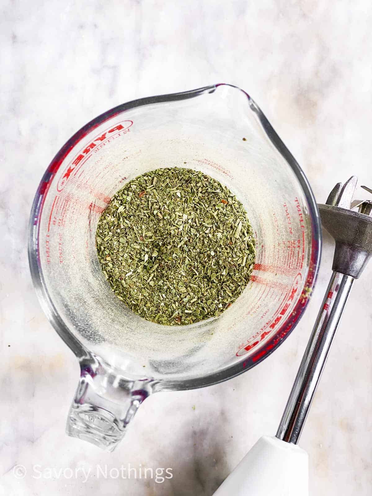 homemade Italian seasoning in glass measuring jug next to an immersion blender