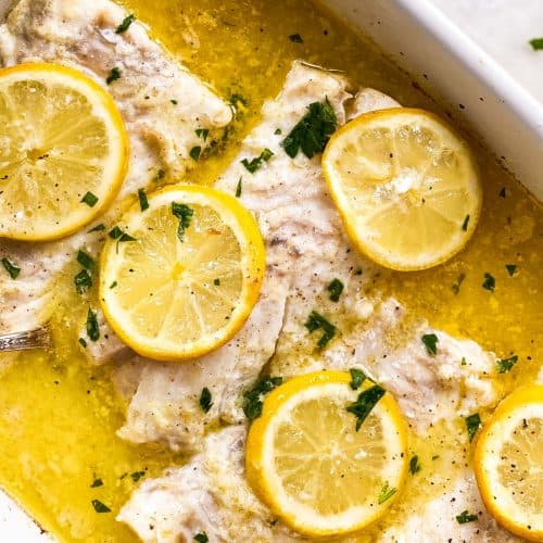 overhead view of four cod loin fillets in white casserole dish with lemon sauce and lemon slices