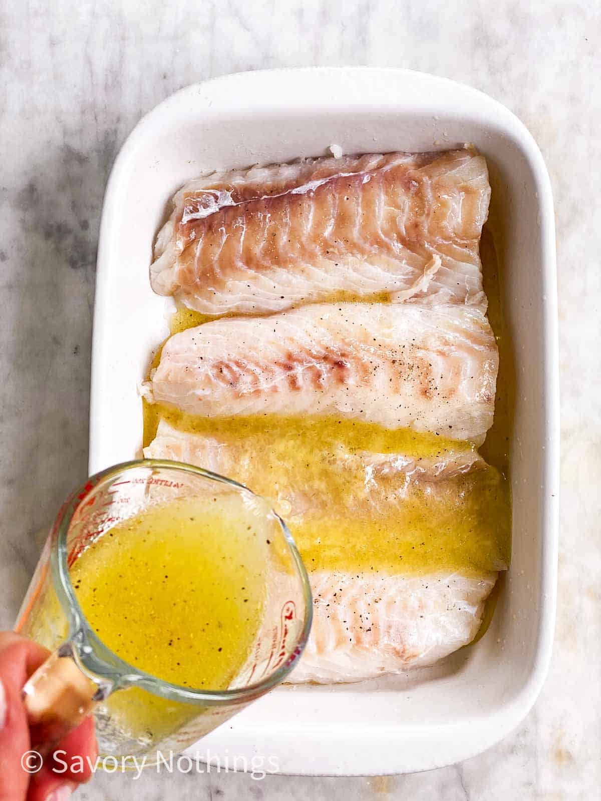 female hand pouring lemon sauce over cod loin fillets in white casserole dish