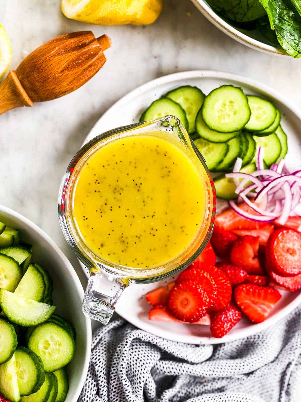 poppy seed salad dressing in glass measuring jug surrounded by salad ingredients