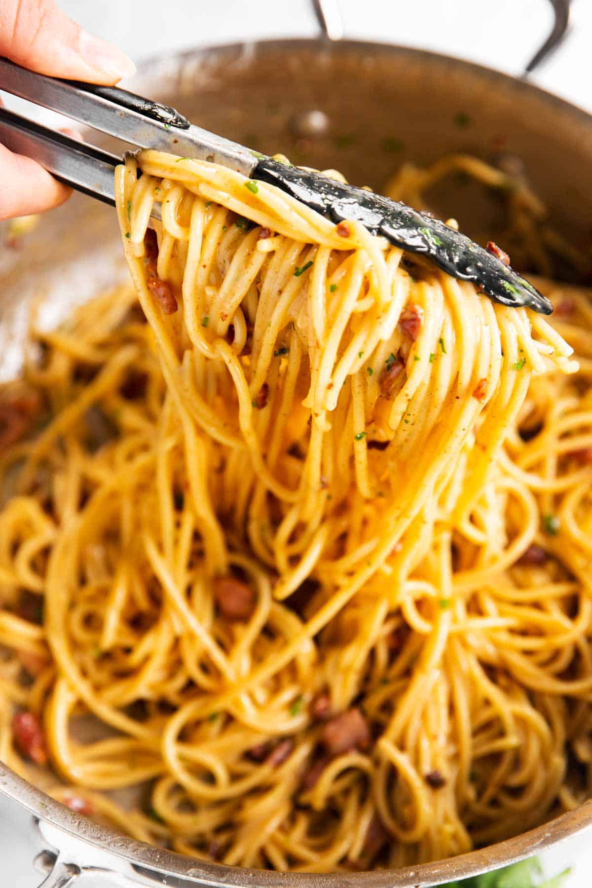 pulling spaghetti carbonara from stainless steel pan with kitchen tongs