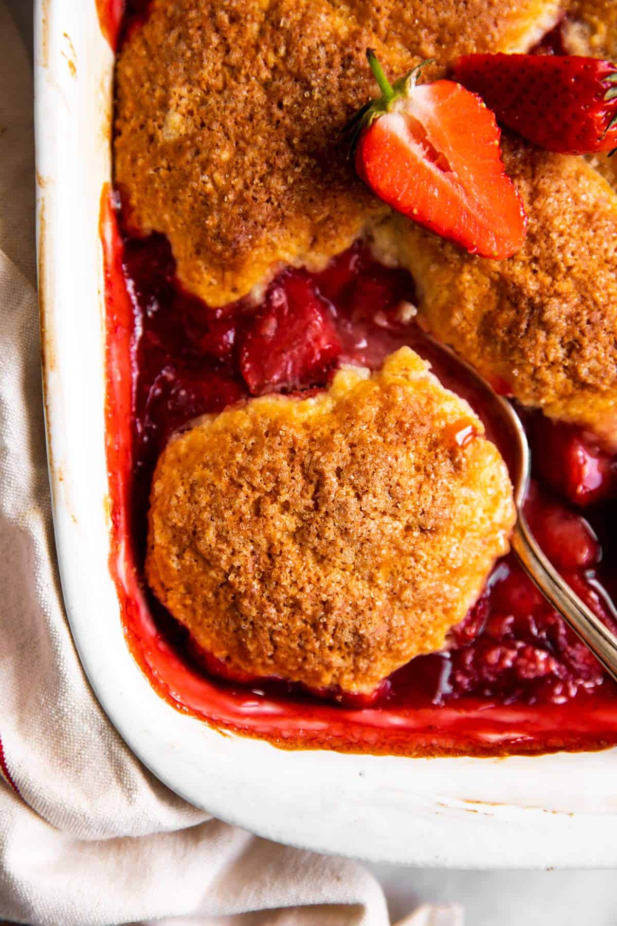 overhead slice up view of strawberry cobbler in white dish with silver spoon