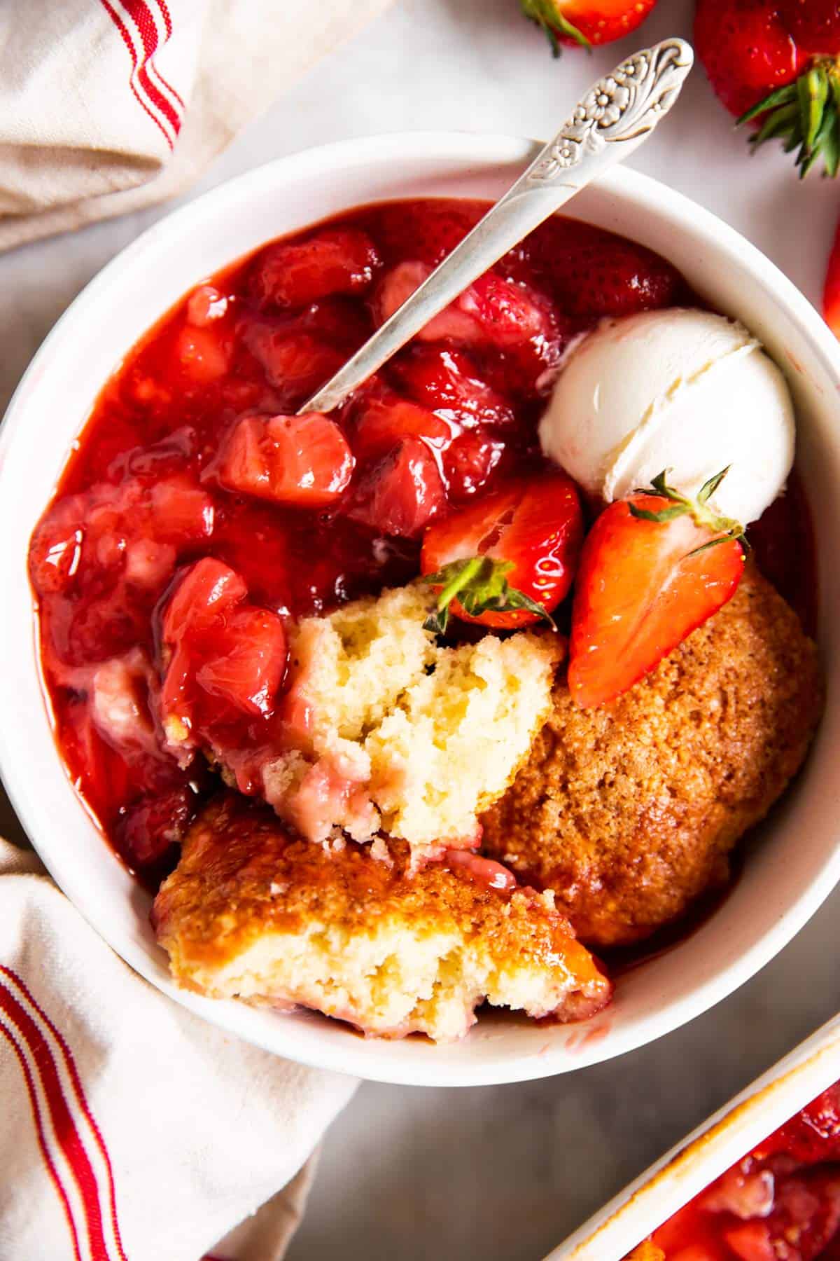 overhead view of strawberry cobbler in white bowl with ice cream