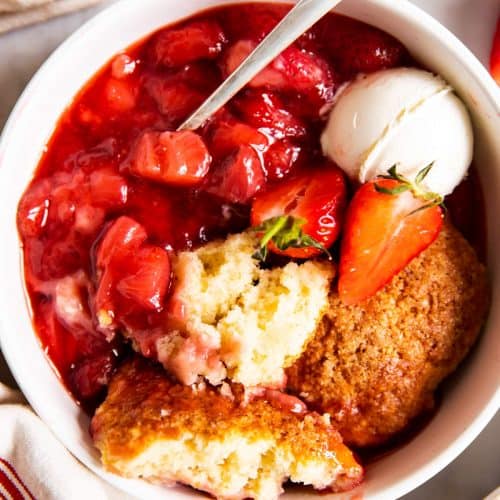 overhead view of strawberry cobbler in white bowl with ice cream