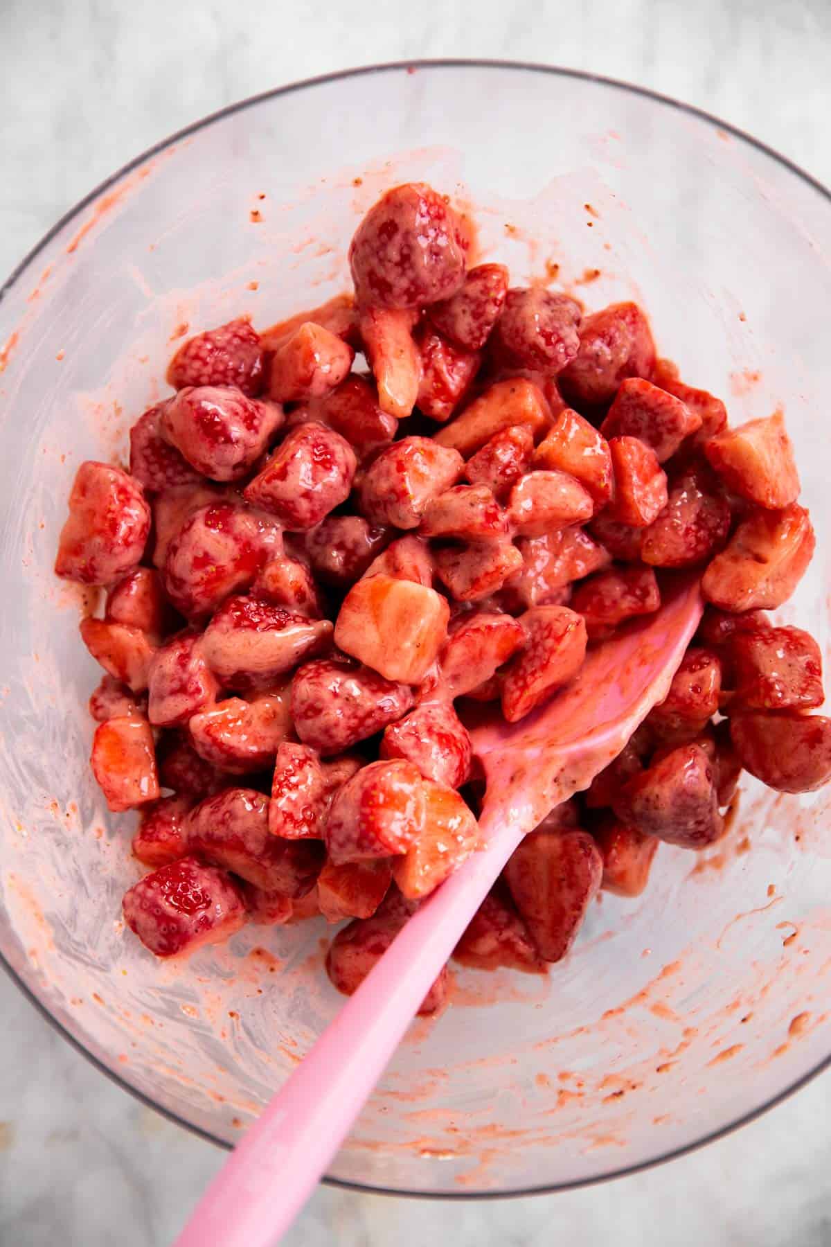 strawberry cobbler filling in glass bowl with pink rubber spatula