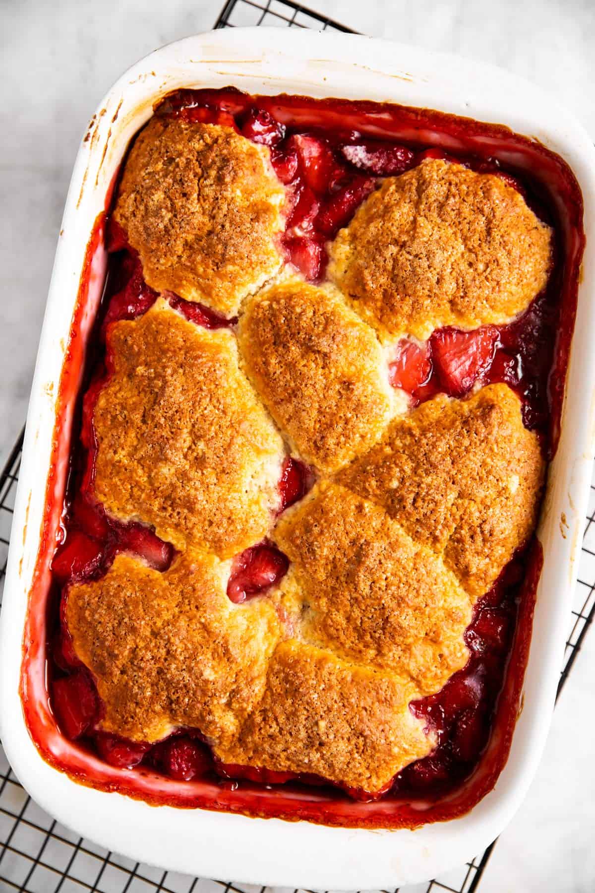 baked strawberry cobbler in white rectangular casserole dish on top of black cooling rack