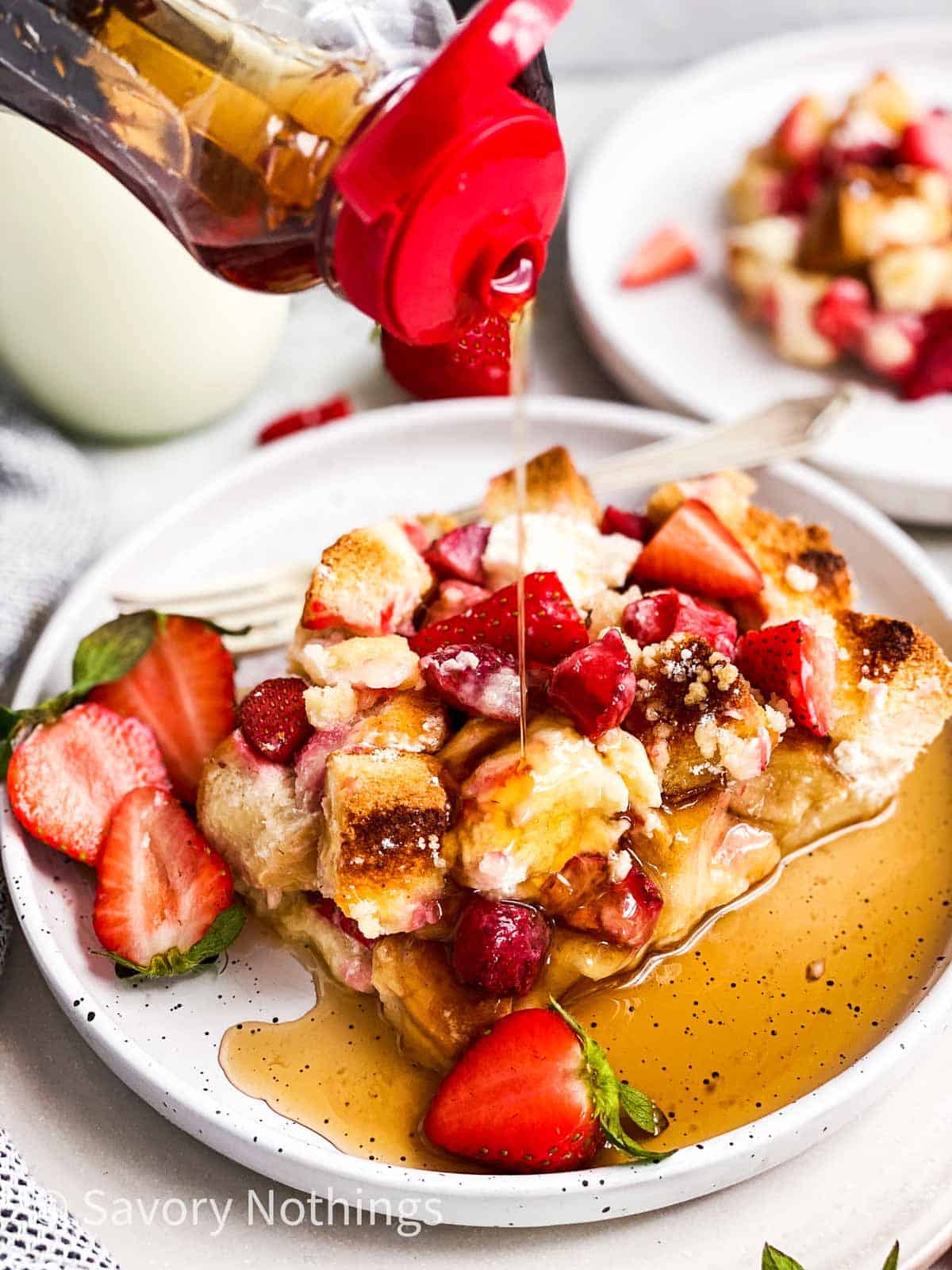 syrup pouring over slice of strawberry French toast casserole on white plate