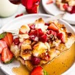 syrup pouring over slice of strawberry French toast casserole on white plate