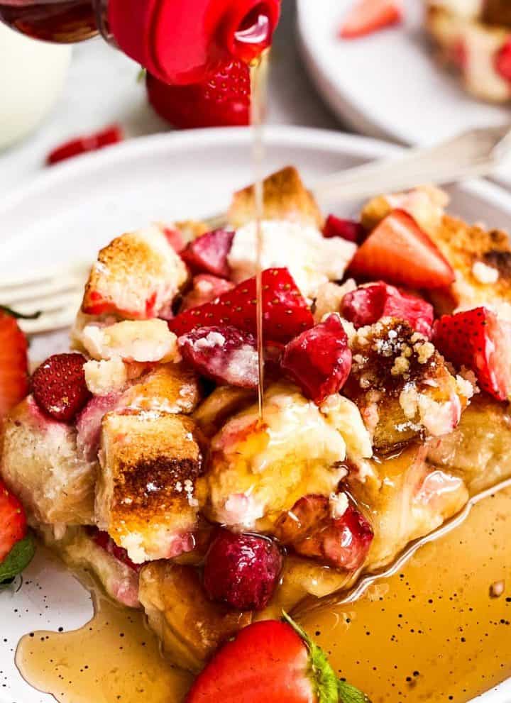 syrup pouring over slice of strawberry French toast casserole on white plate