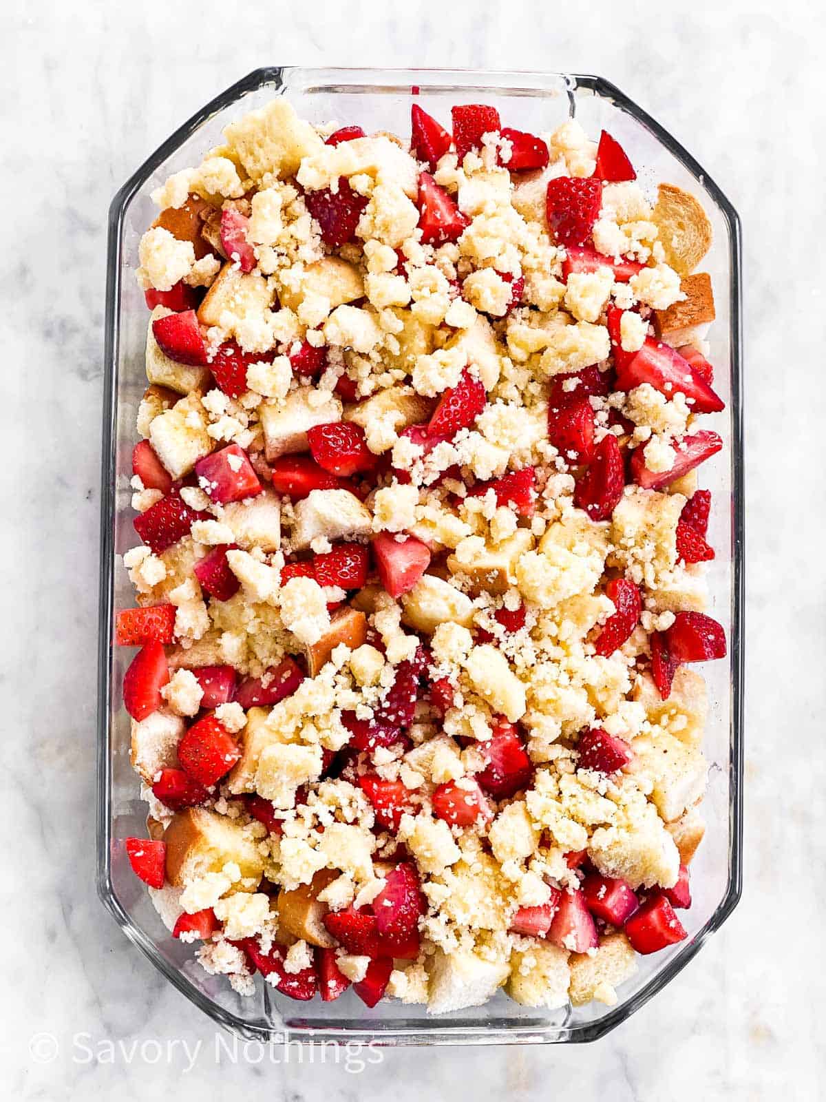 unbaked strawberry French toast casserole in glass dish sitting on marble surface, topped with streusel