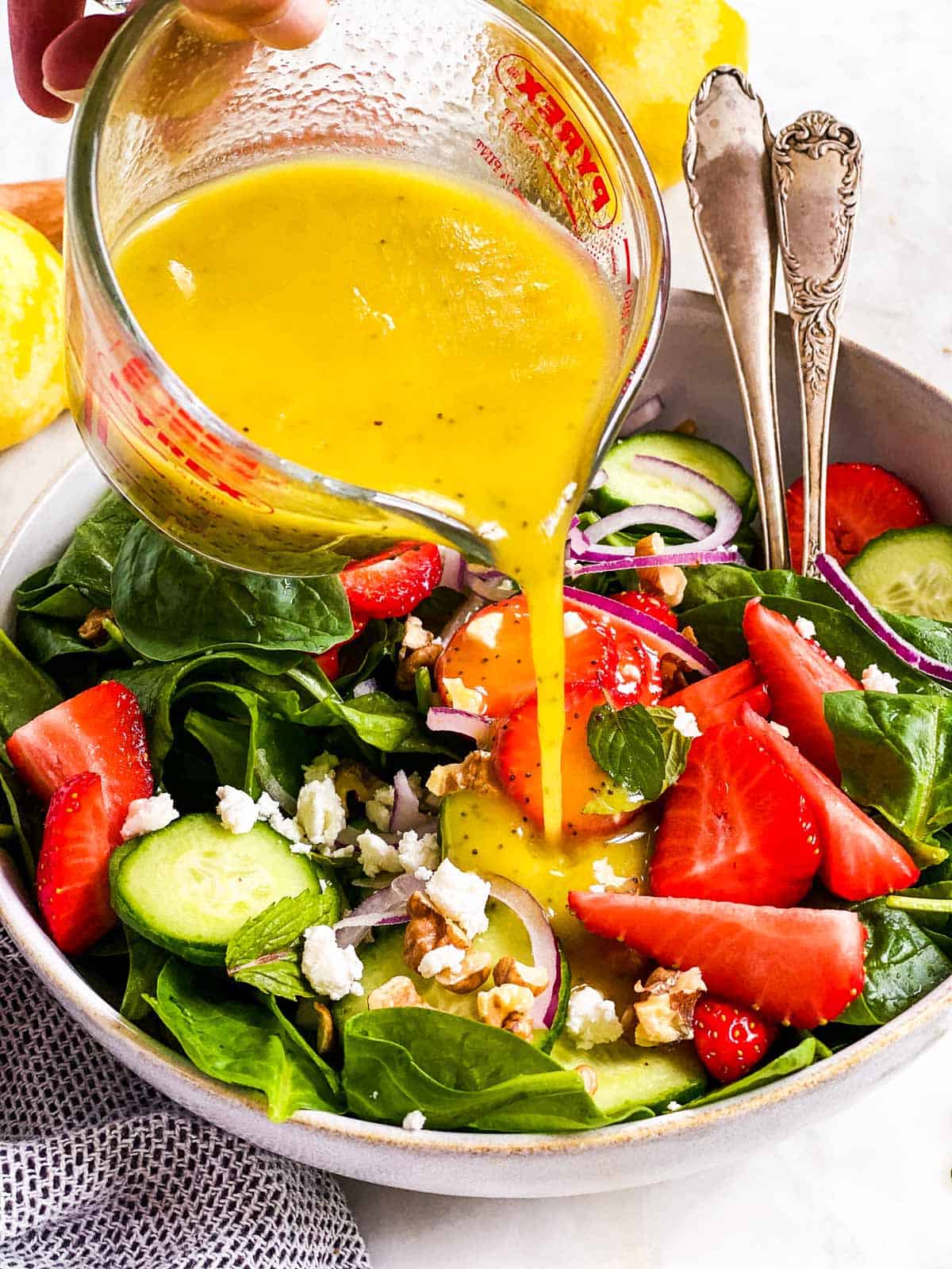 lemon poppy seed salad dressing pouring over strawberry spinach salad from glass measuring jug