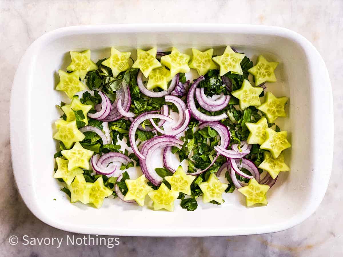 chopped herbs, sliced red onion and cucumber star cutouts in rectangular white dish