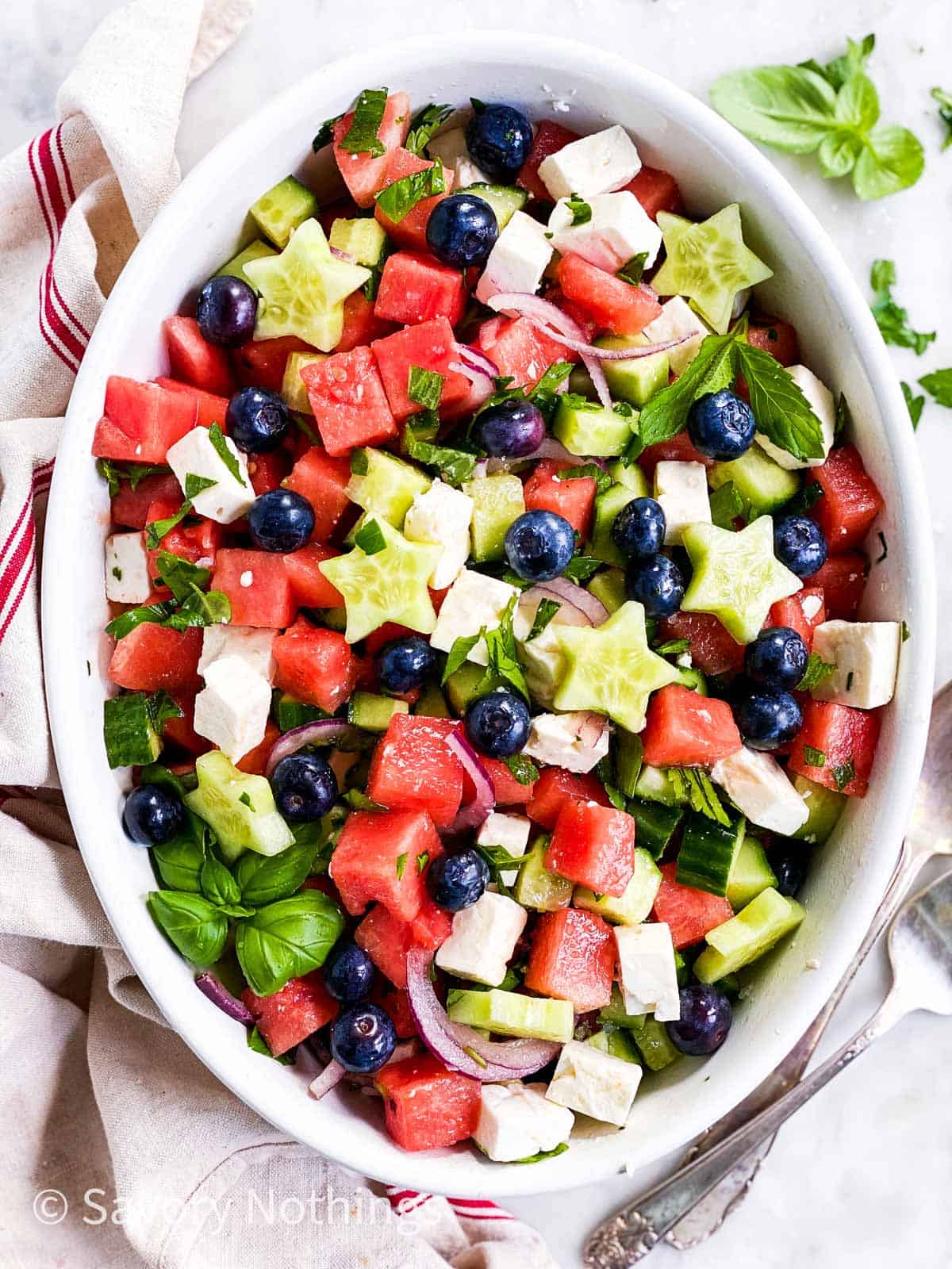 watermelon and feta salad with blueberries and cucumber stars in white oval dish