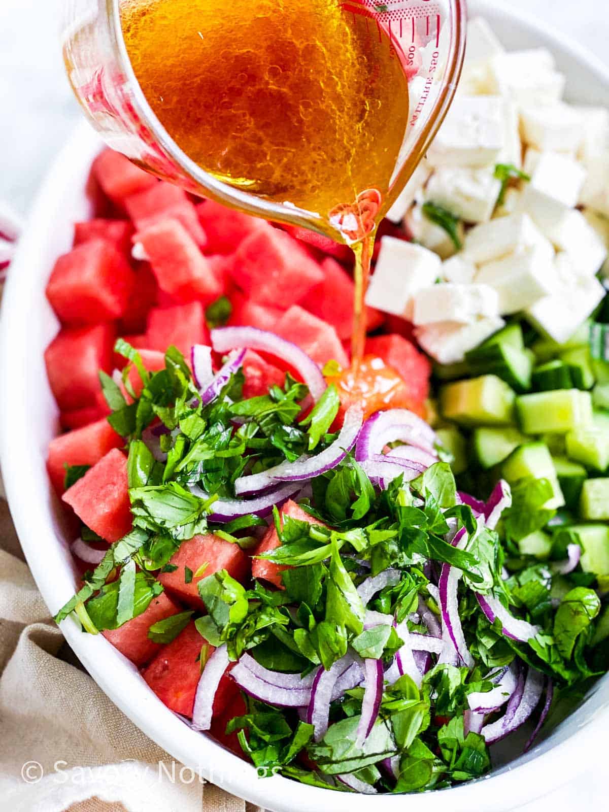 vinaigrette pouring from glass jug over ingredients for watermelon salad