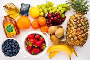 Ingredients for classic fresh fruit salad on a white marble surface.