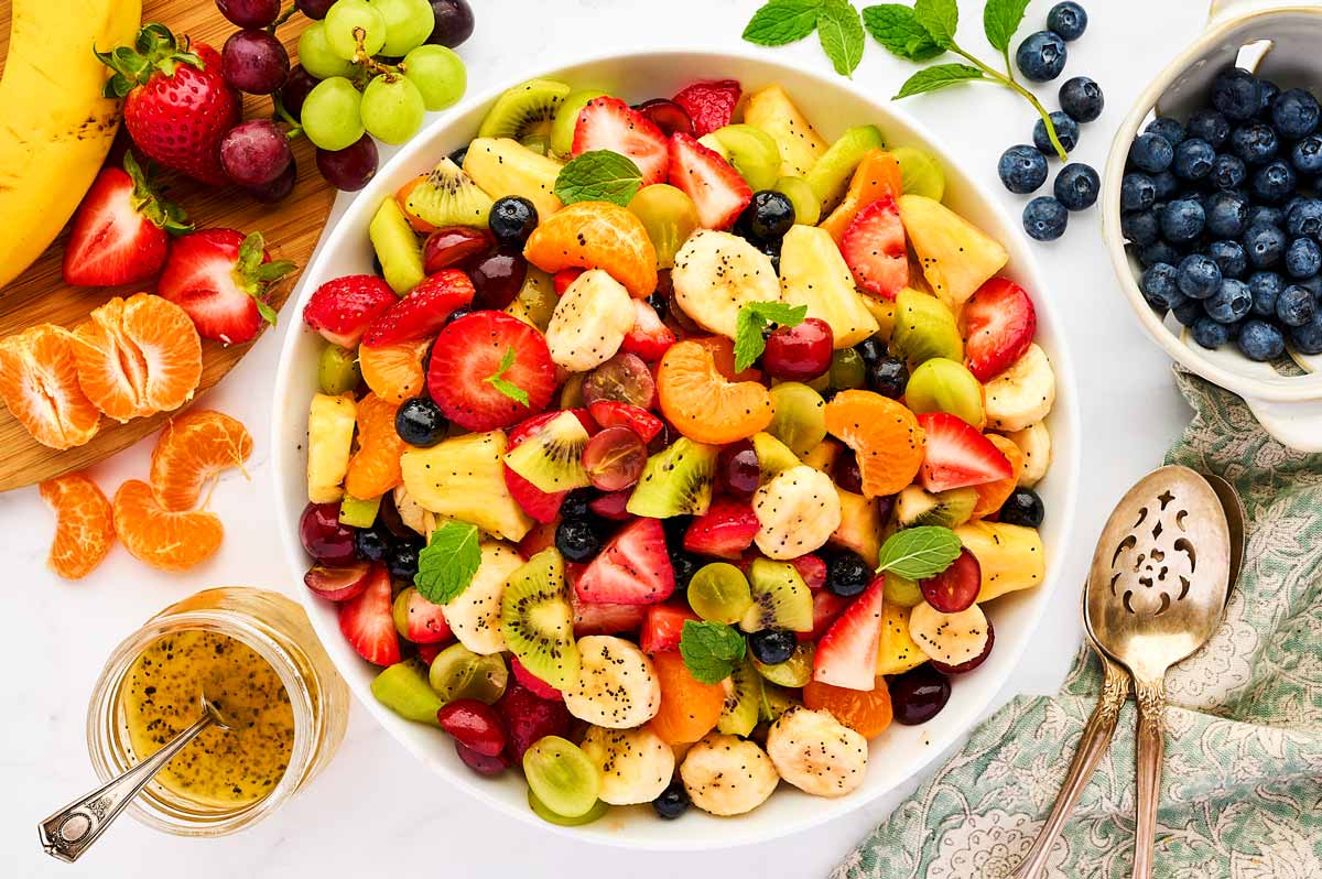 Bowl of fresh fruit salad surrounded by more fresh fruit.
