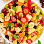 Bowl of fresh fruit salad surrounded by more fresh fruit.