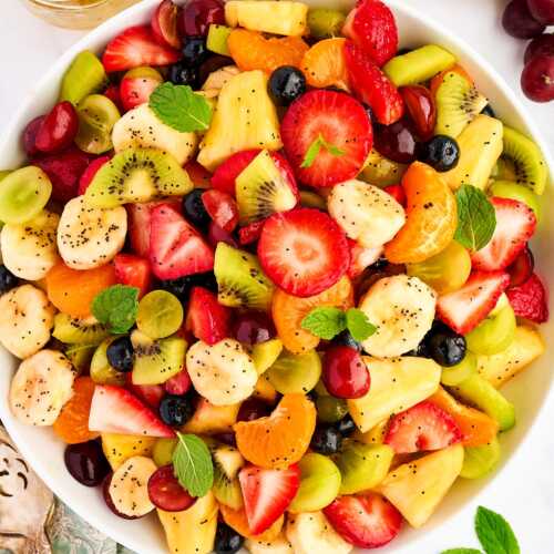 Bowl of fresh fruit salad surrounded by more fresh fruit.