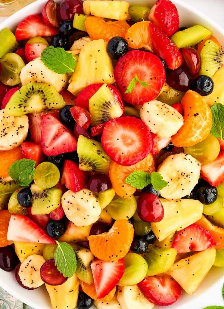 Bowl of fresh fruit salad surrounded by more fresh fruit.
