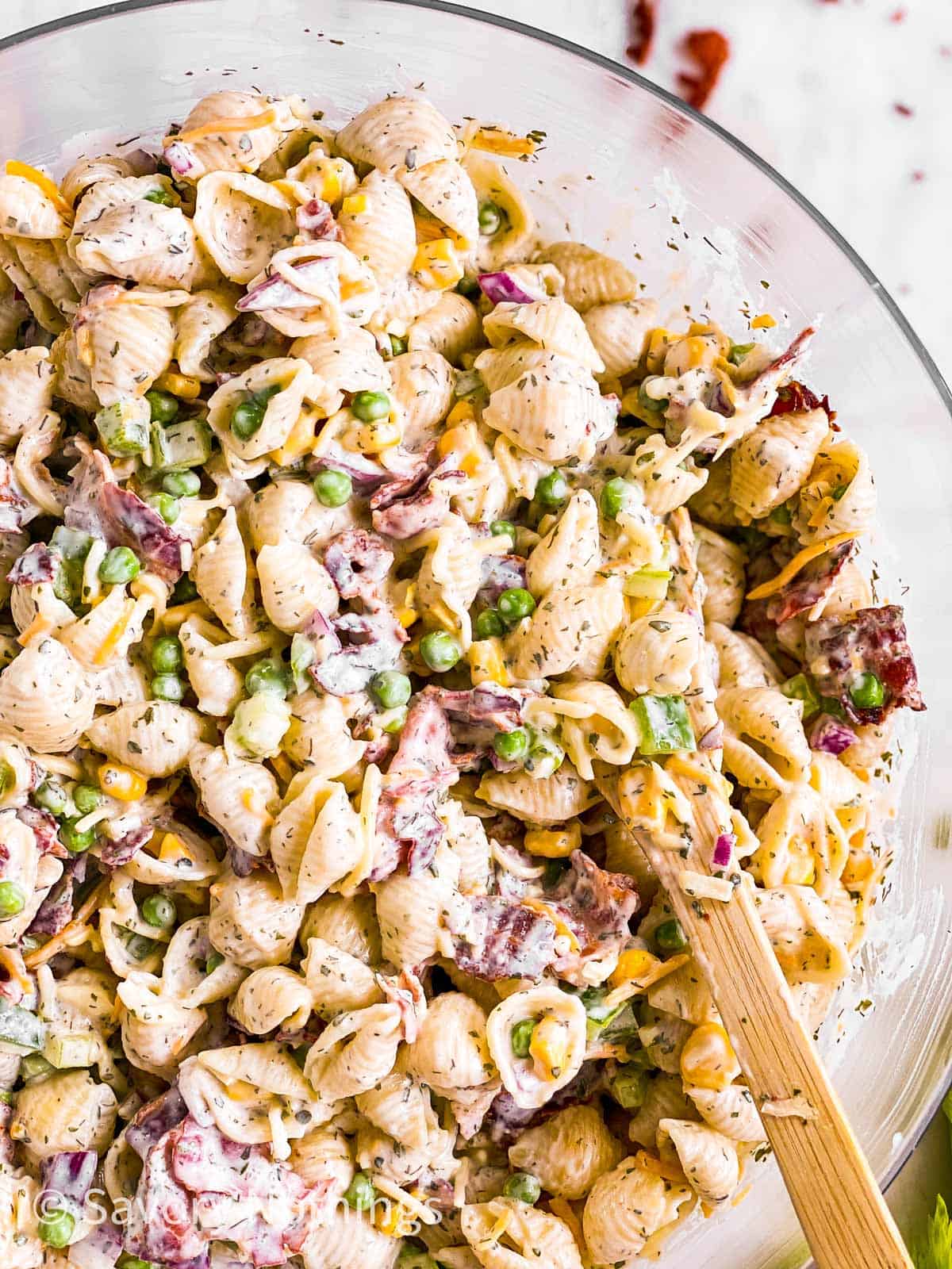 overhead close up view of wooden spoon in bacon ranch pasta salad in glass bowl 