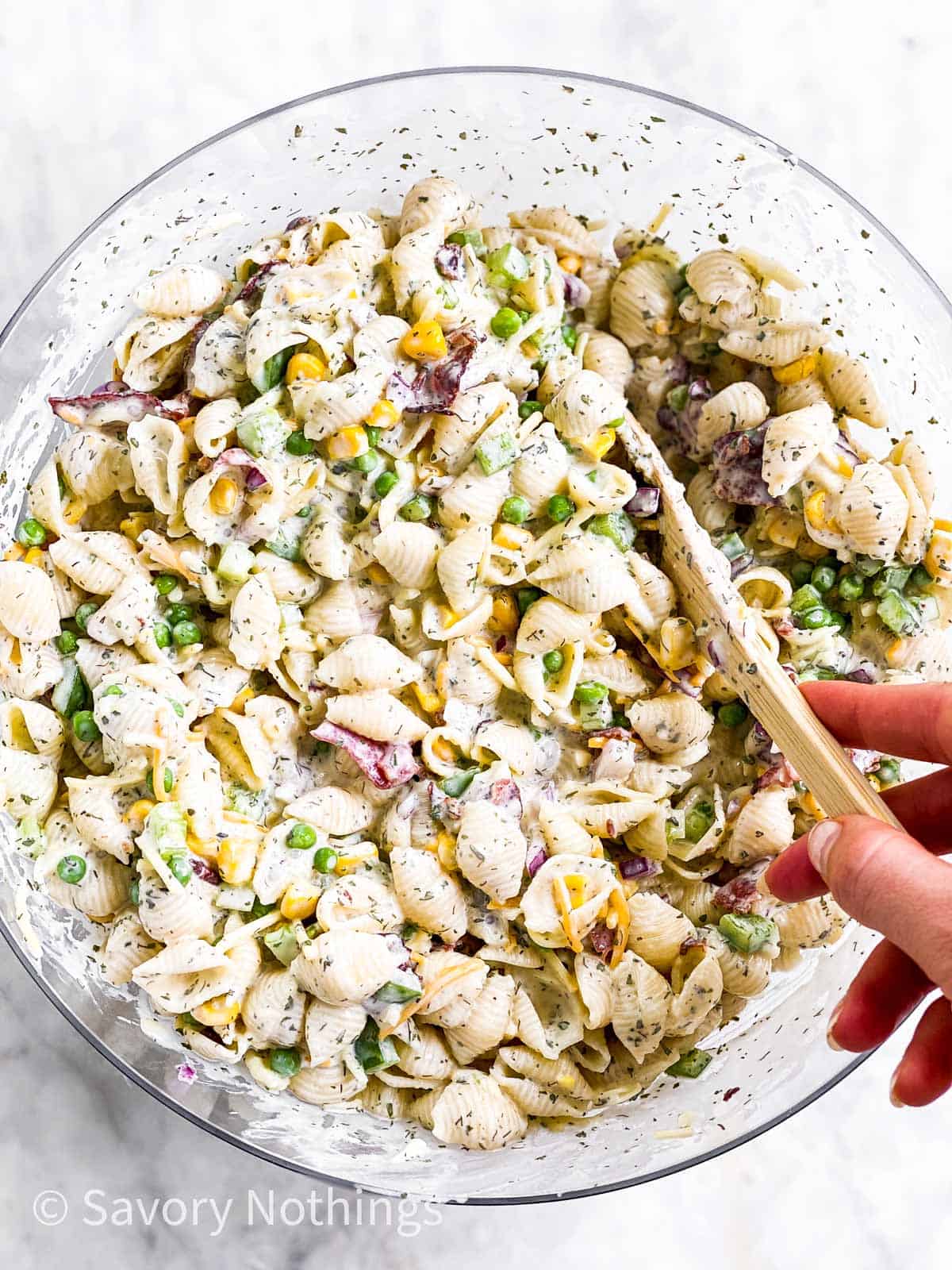female hand stirring ranch pasta salad in glass bowl