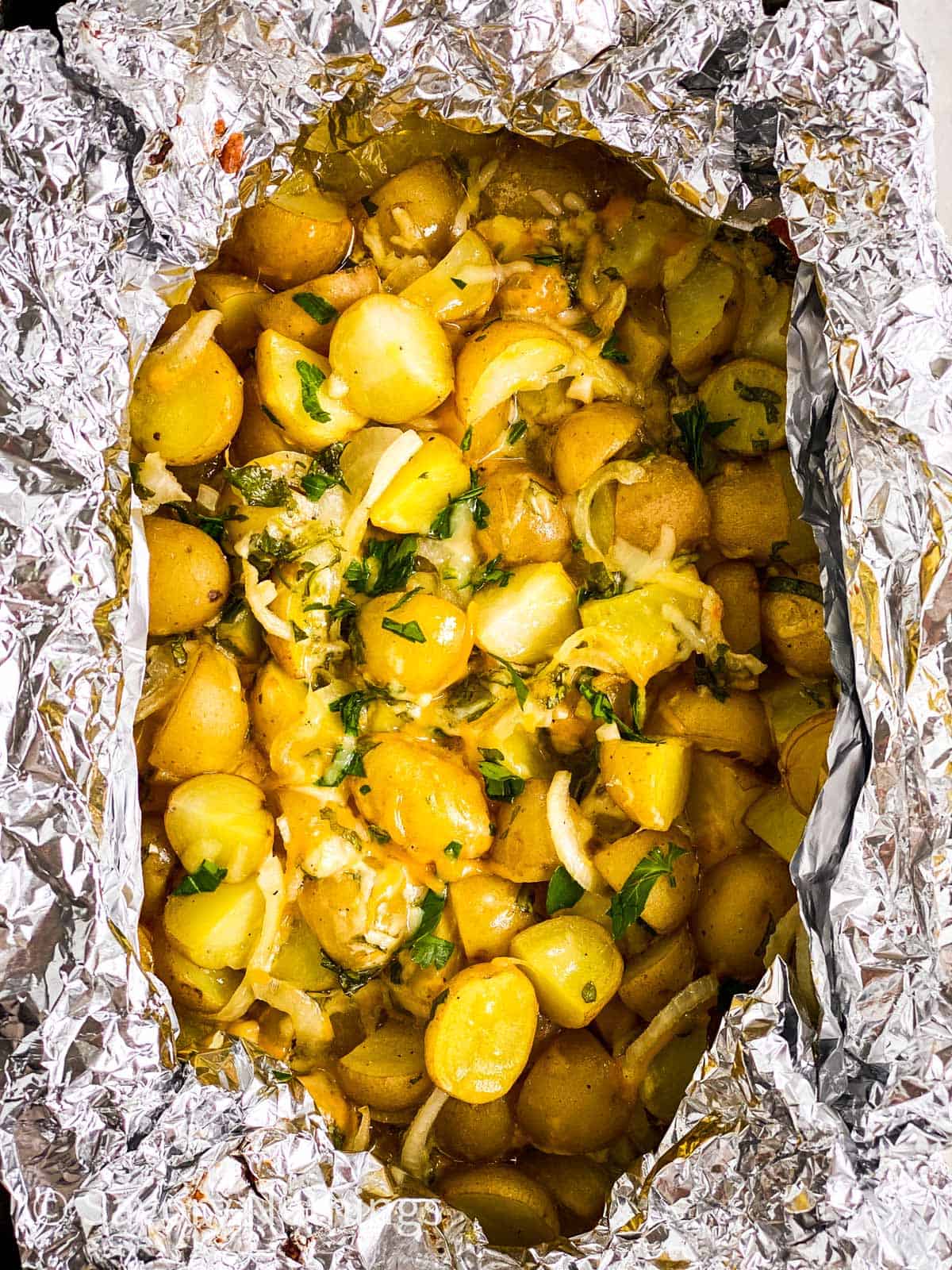 close up photo of cheesy campfire potatoes in foil pouch