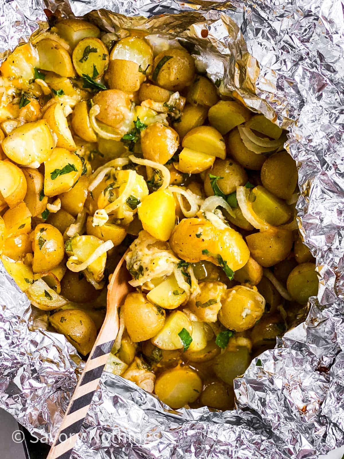 overhead view of cheesy campfire potatoes in foil packet with disposable fork stuck inside