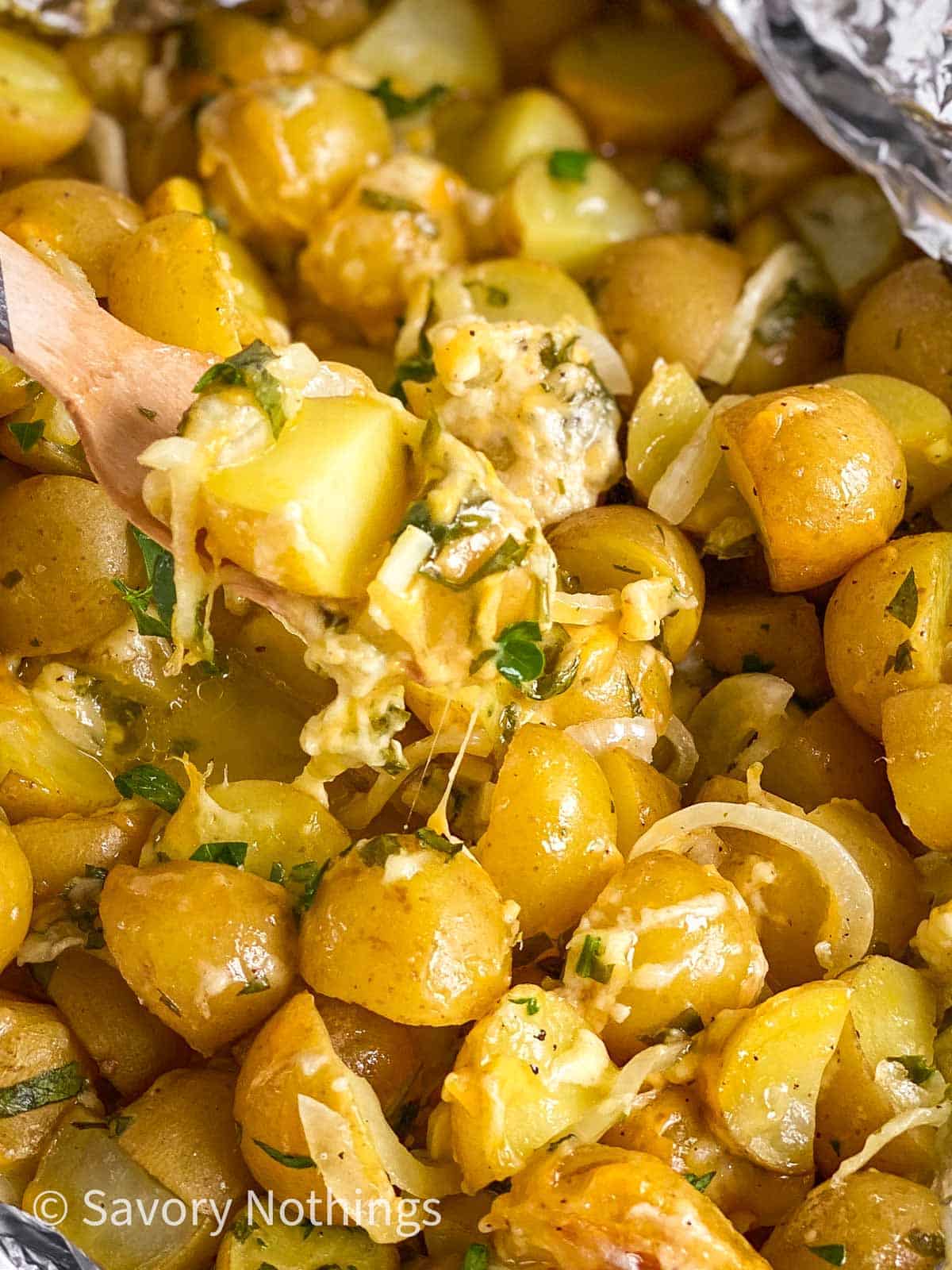 fork scooping up cheesy campfire potatoes from opened foil pouch