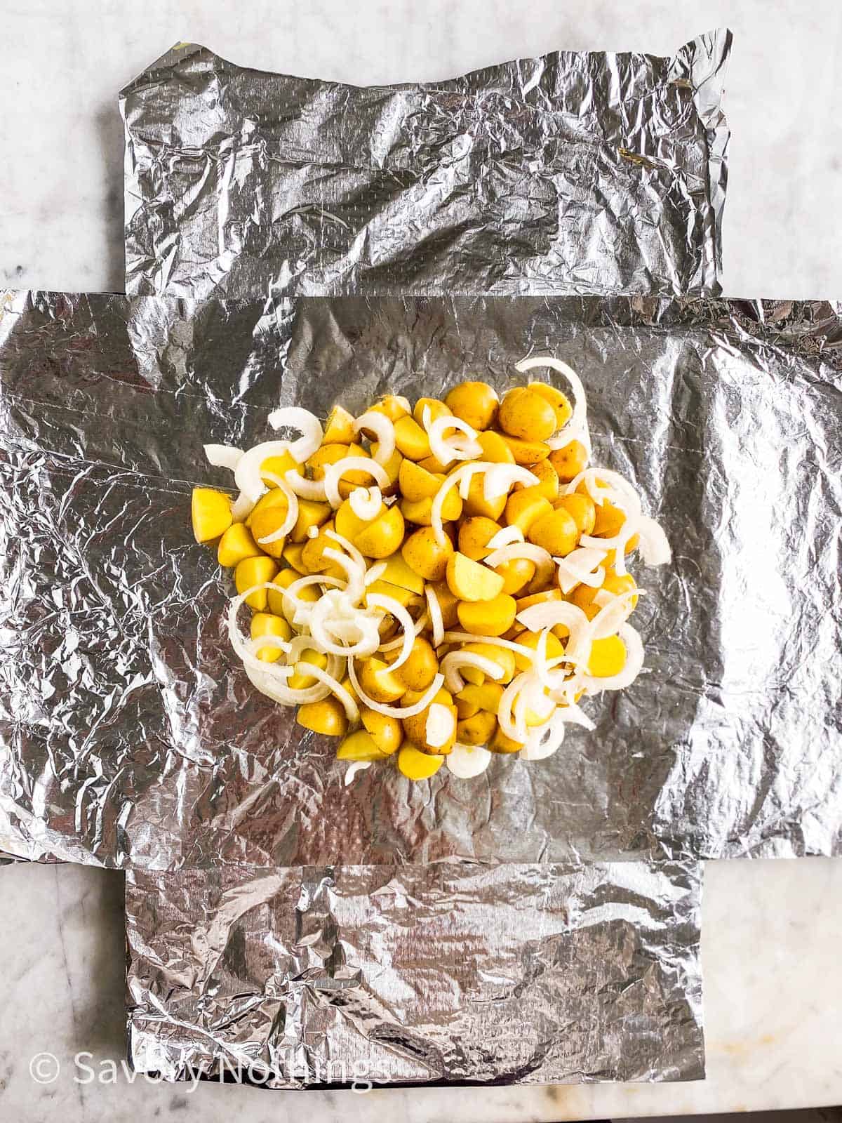 cut up baby potatoes and onions on aluminium foil